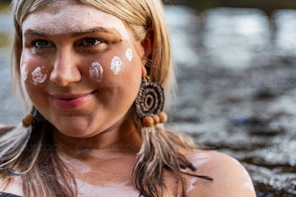 Close up portrait of aboriginal woman with woven earring and ochre paint on face - Australian Stock Image