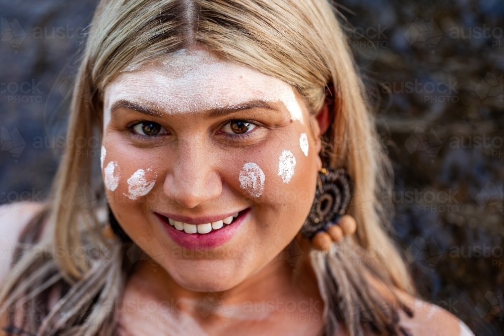 Close up portrait of aboriginal woman with woven earring and ochre paint on face - Australian Stock Image