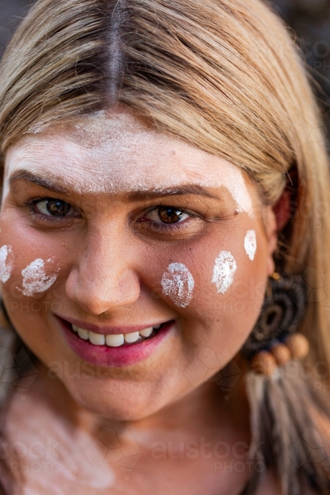 Close up portrait of aboriginal woman with woven earring and ochre paint on face - Australian Stock Image