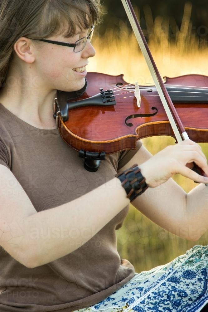 Image of Close up portrait of girl playing violin outdoors in a paddock ...
