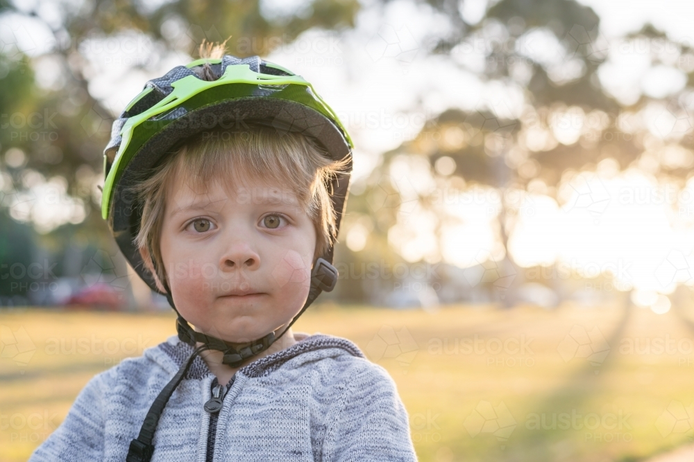 Close-up portrait of little boy wearing bicycle helmet at sunset - Australian Stock Image
