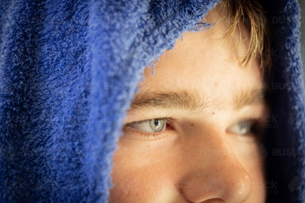 Close up portrait of teen boy's blue eyes under hooded towel - Australian Stock Image