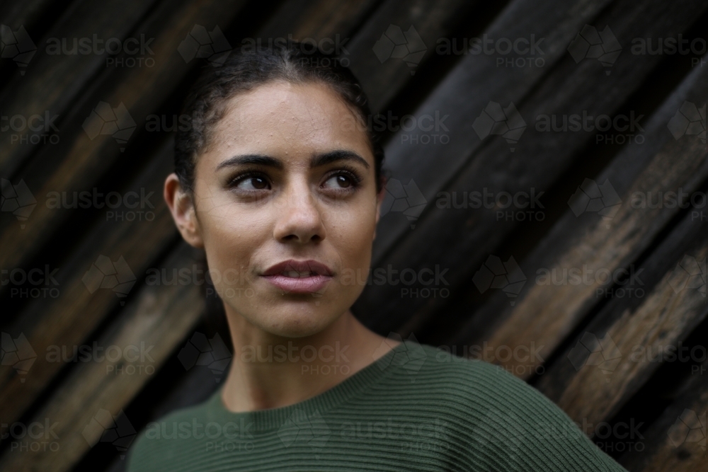 Close up portrait of young Fijian woman standing in front of textured wooden panels - Australian Stock Image