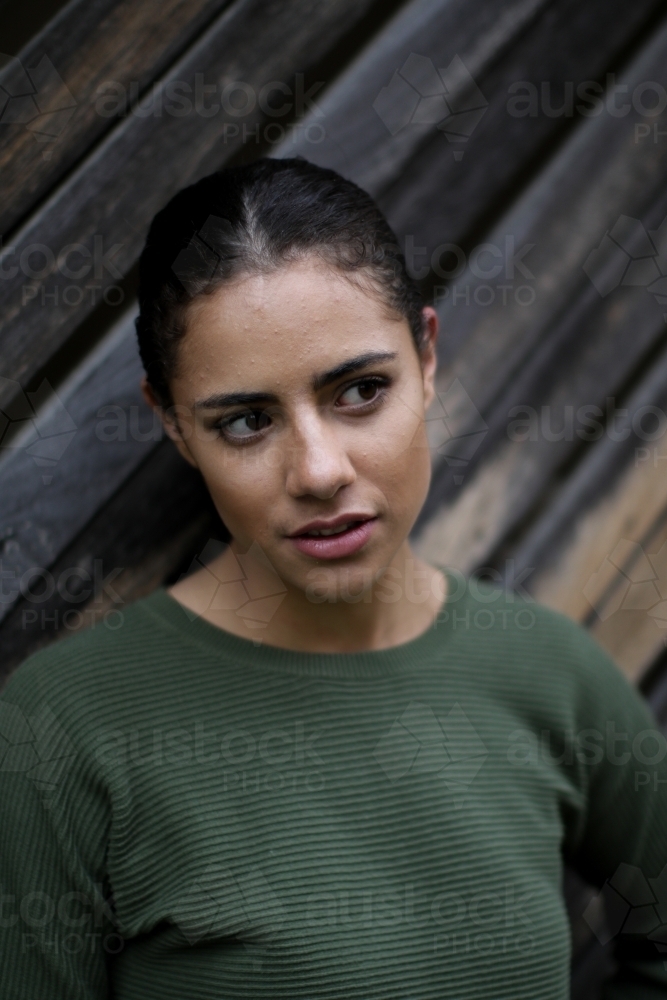 Close up portrait of young Fijian woman standing in front of textured wooden panels - Australian Stock Image