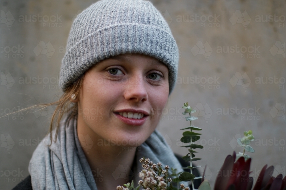 Close up portrait of young girl in a beanie holding a floral arrangement - Australian Stock Image