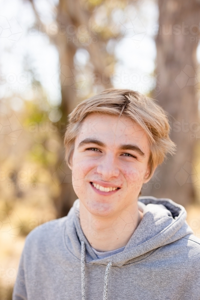 Close up portrait teen boy smiling wearing hoodie in bushland - Australian Stock Image