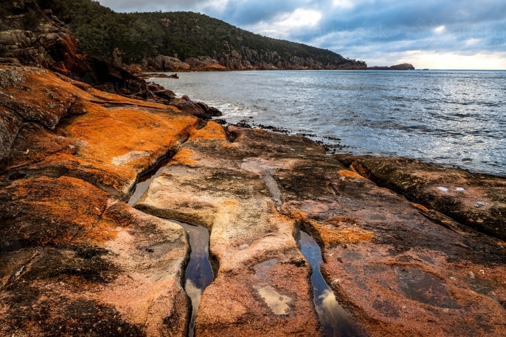 Close up shot drainage pattern rock by the sea with mountain background - Australian Stock Image