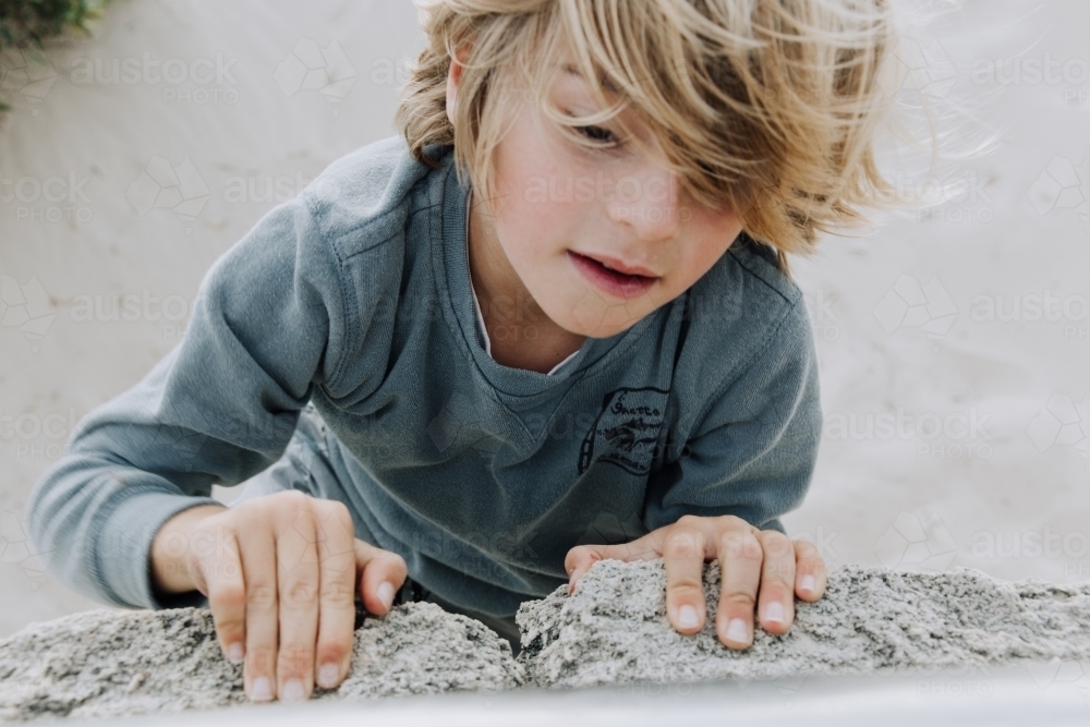 Close up shot of a boy climbing on a pile of rocks. - Australian Stock Image