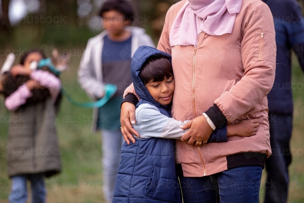 Close up shot of a boy wearing blue coat hugging a woman wearing pink sweater and hijab - Australian Stock Image