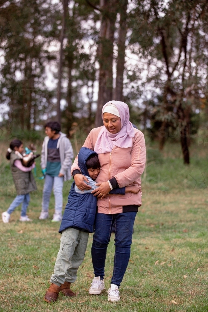 Close up shot of a boy wearing blue coat hugging a woman wearing pink sweater and hijab - Australian Stock Image
