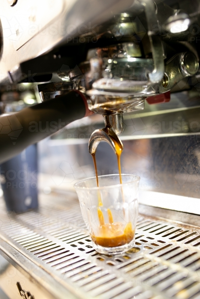 Close up shot of a coffee machine pouring coffee to a medium sized glass cup on a coffee counter - Australian Stock Image