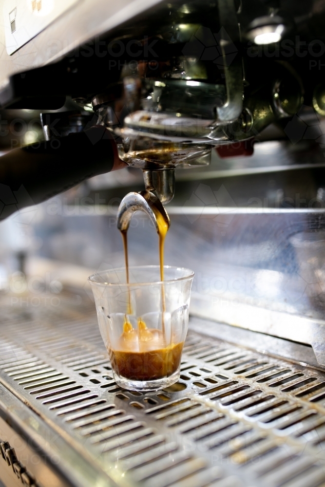 Close up shot of a coffee machine pouring coffee to a medium sized glass cup on a coffee counter - Australian Stock Image
