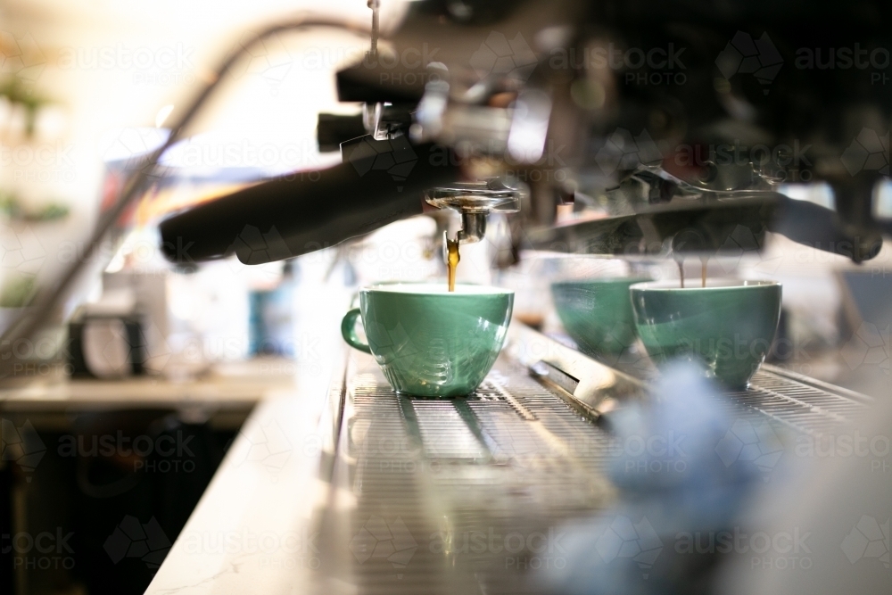 Close up shot of a coffee machine pouring coffee to a medium sized green mug on a coffee counter - Australian Stock Image