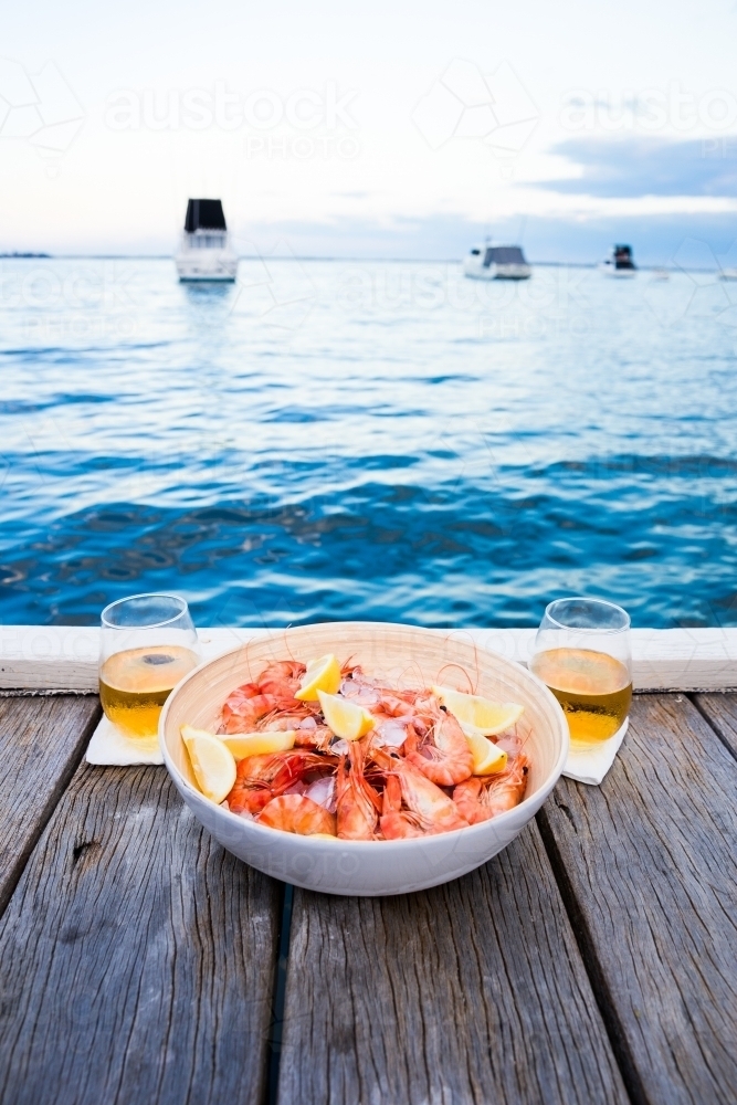 Close up shot of a lemon butter shrimp in a white bowl on the pool side with two glasses of whiskey - Australian Stock Image
