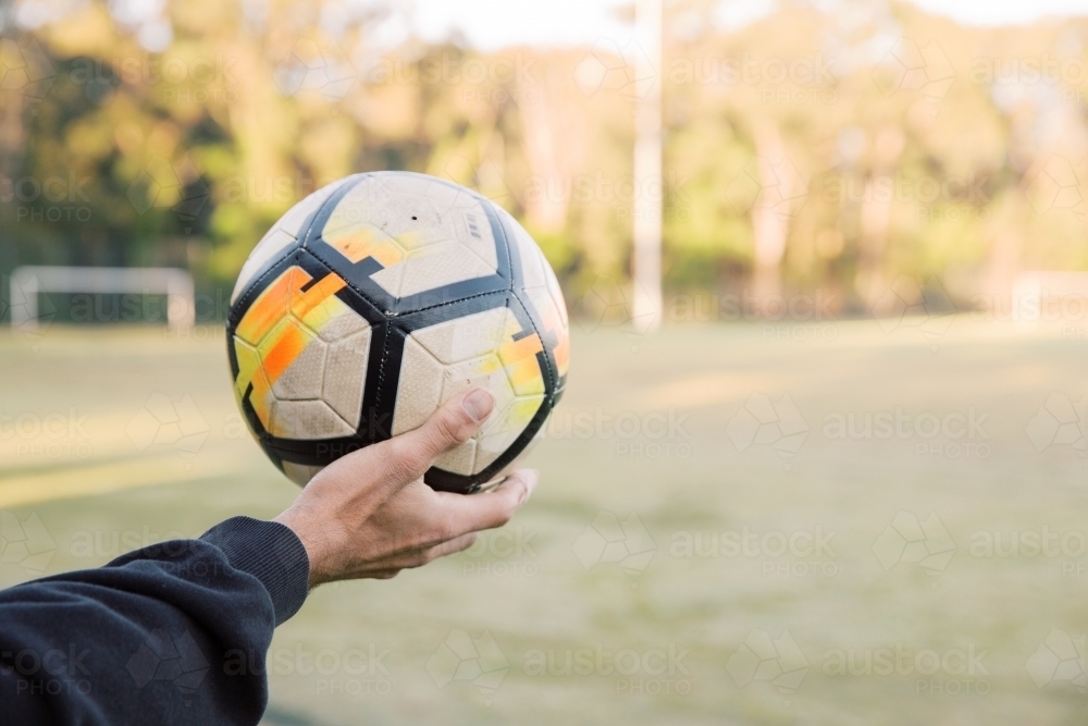 Close up shot of a man holding a soccer ball in the field with a blurry background - Australian Stock Image