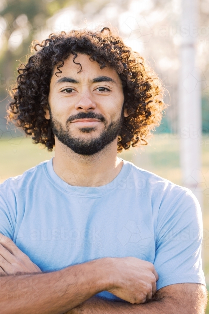 close up shot of a man smiling with curly hair and beard showing his dimples and wearing blue shirt - Australian Stock Image