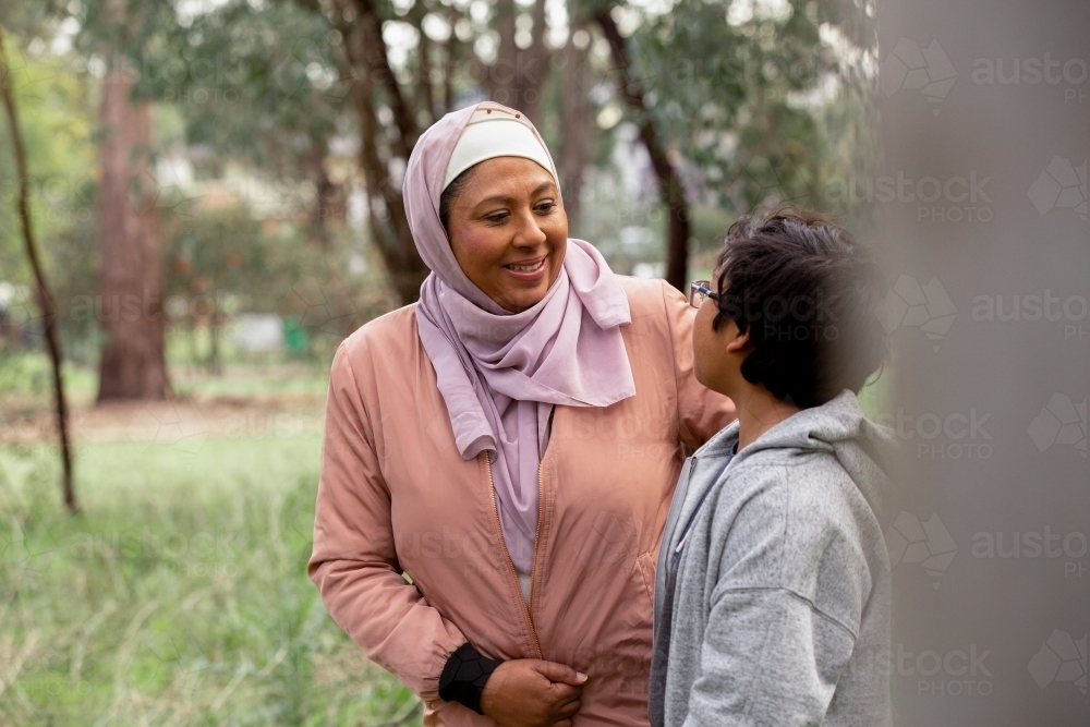 Close up shot of a middle aged woman wearing pink hijab talking to a boy with curly hair and glasses - Australian Stock Image