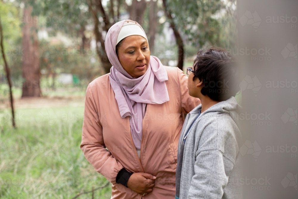 Close up shot of a middle aged woman wearing pink hijab talking to a boy with curly hair and glasses - Australian Stock Image