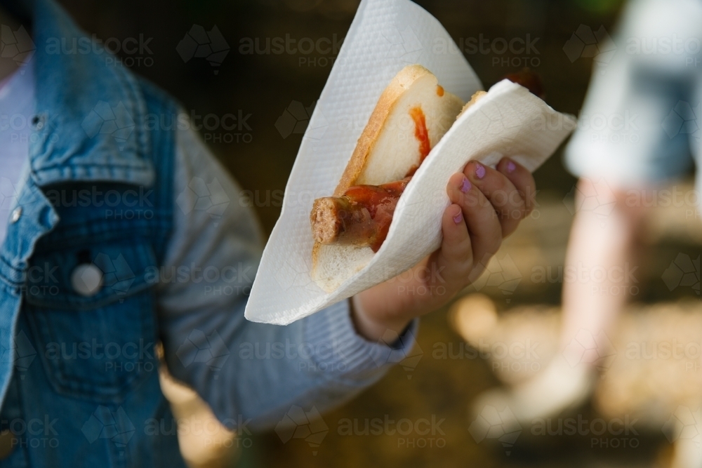 Close up shot of a person holding a sausage sandwich with ketchup in a sandwich tissue - Australian Stock Image