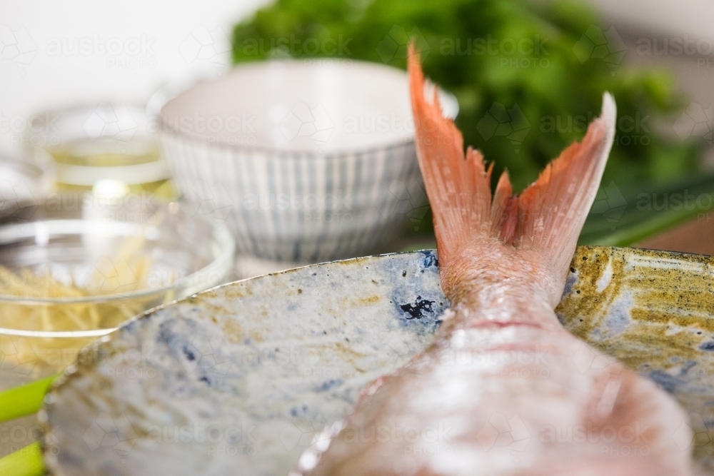 Close up shot of a red fish on a plate with blurry background of saucers and green vegetable - Australian Stock Image