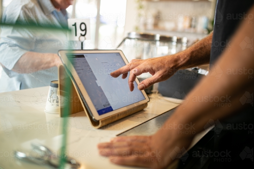 Close up shot of a tablet on the order counter being clicked by the barista's finger - Australian Stock Image