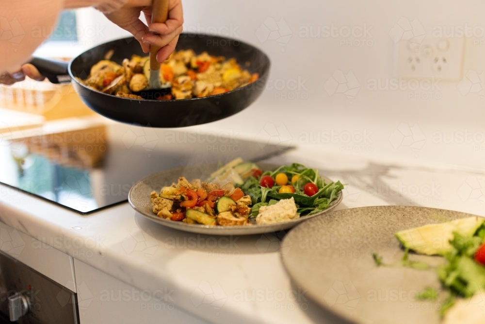 Close up shot of a person serving up meal from pan to plate - Australian Stock Image