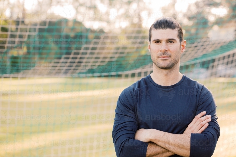 Close up shot of a young man standing on the soccer field with crossed arms near the soccer net - Australian Stock Image