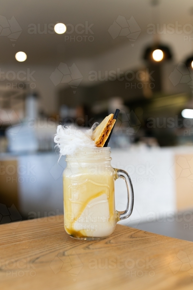 Close up shot of coffee in a mason jar with caramel on the sides, a fairy floss and biscuit on top - Australian Stock Image