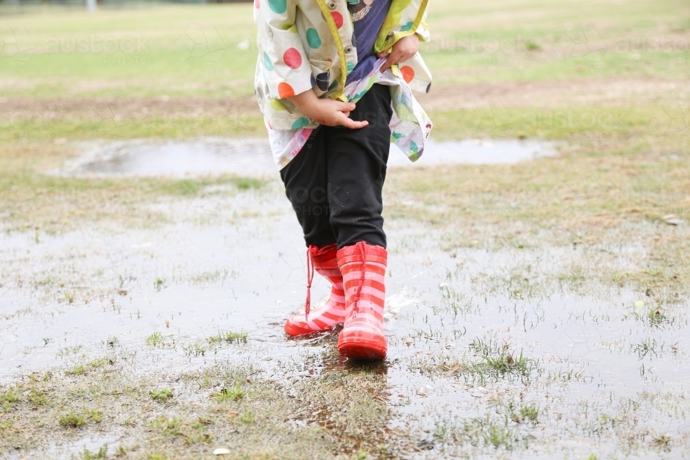 Close-up shot of girl's  feet in red gumboots standing in puddle - Australian Stock Image