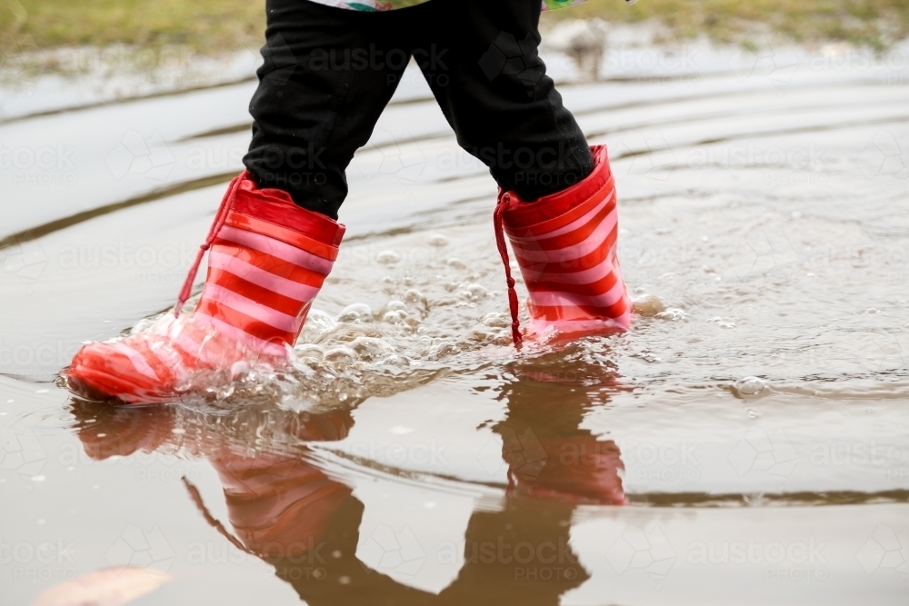 Close-up shot of girl's feet in red gumboots standing in puddle - Australian Stock Image