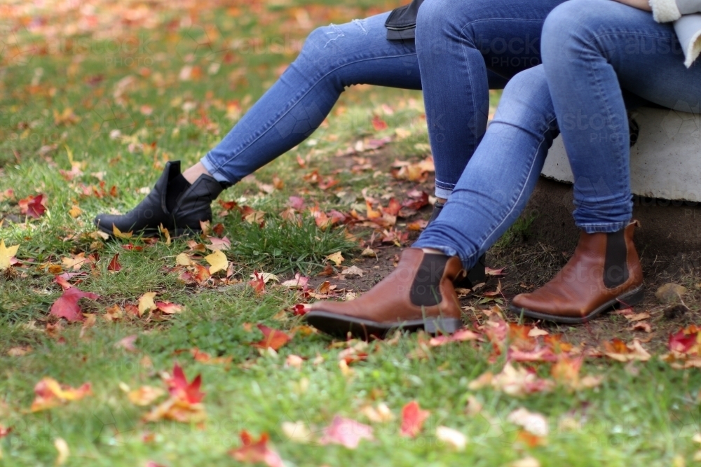 Close up shot of girls legs wearing jeans and boots surrounded by autumn leaves - Australian Stock Image