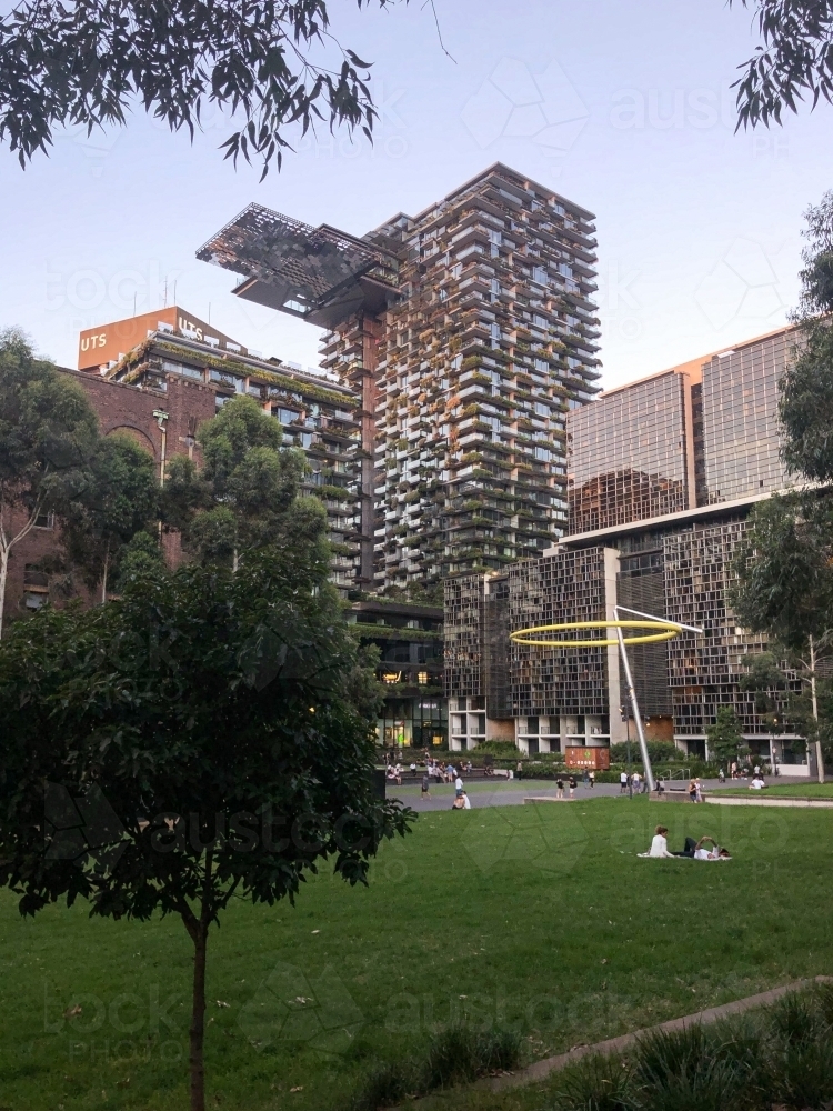 close up shot of high rise buildings with vines and group of people sitting down on a big lawn - Australian Stock Image
