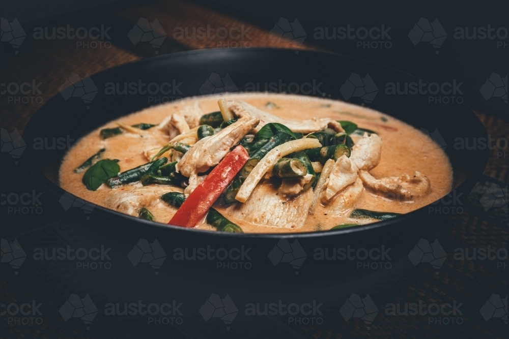 Close up shot of red curry chicken in a black bowl - Australian Stock Image