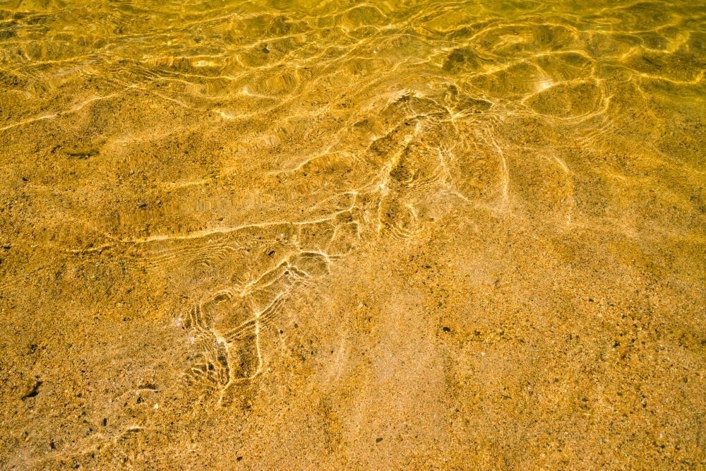 Close up shot of water rippling over yellow sand - Australian Stock Image