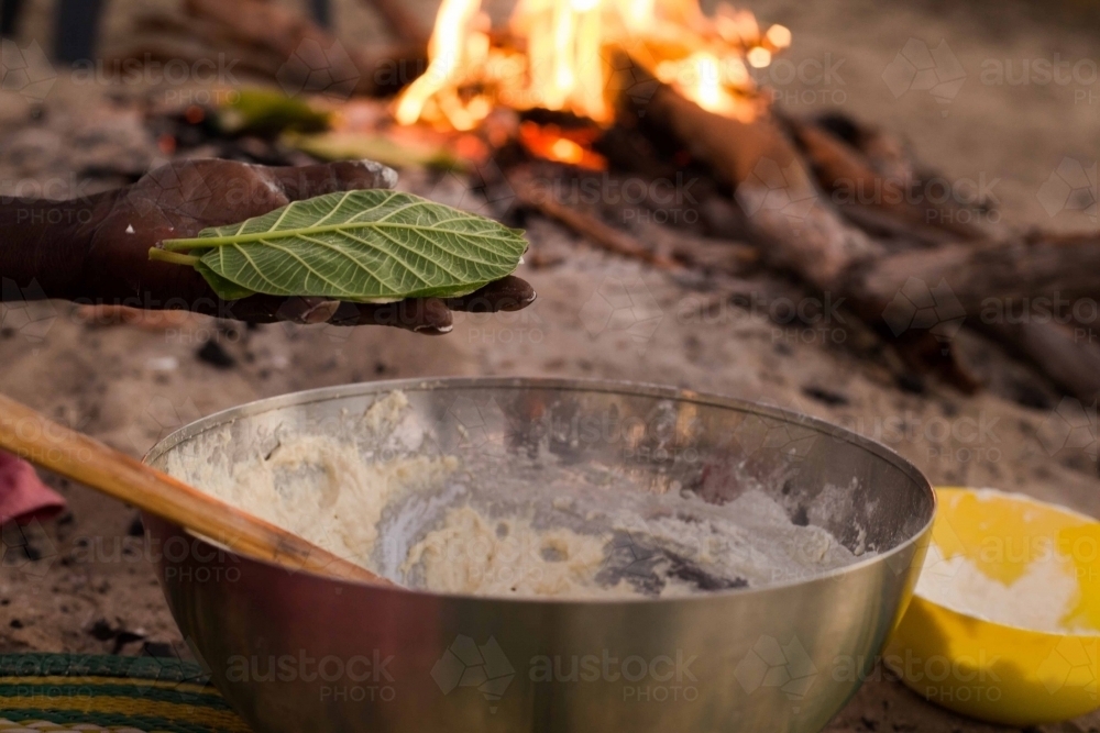 Close up shot of woman holding a leaf with a big bowl of flour on the ground and a flame on the back - Australian Stock Image
