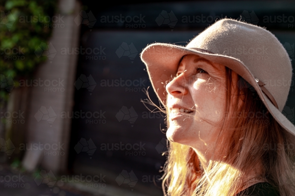 close up shot of woman smiling and looking up wearing a hat and sunlight hitting her face - Australian Stock Image