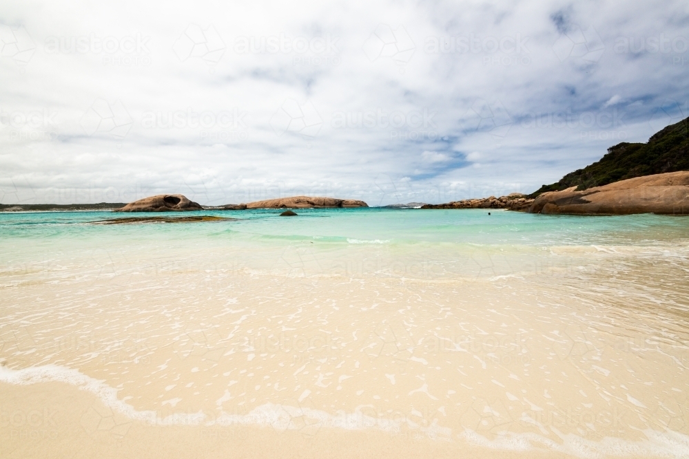 Close up view of water's edge at a pretty cove with swimmer in the distance and islands - Australian Stock Image