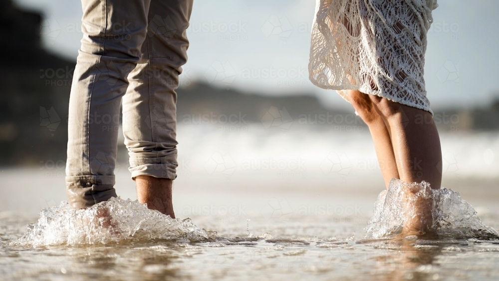Close ups of couples feet standing on beach in water - Australian Stock Image