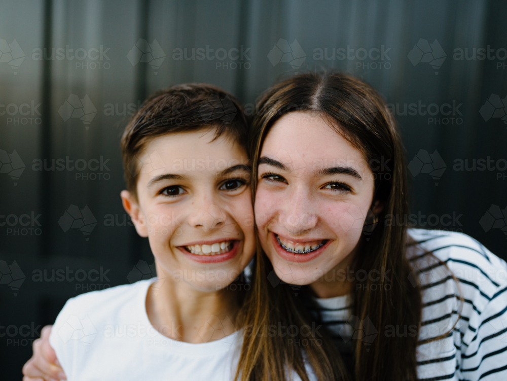 Closeup of brother and sister smiling at the camera. - Australian Stock Image