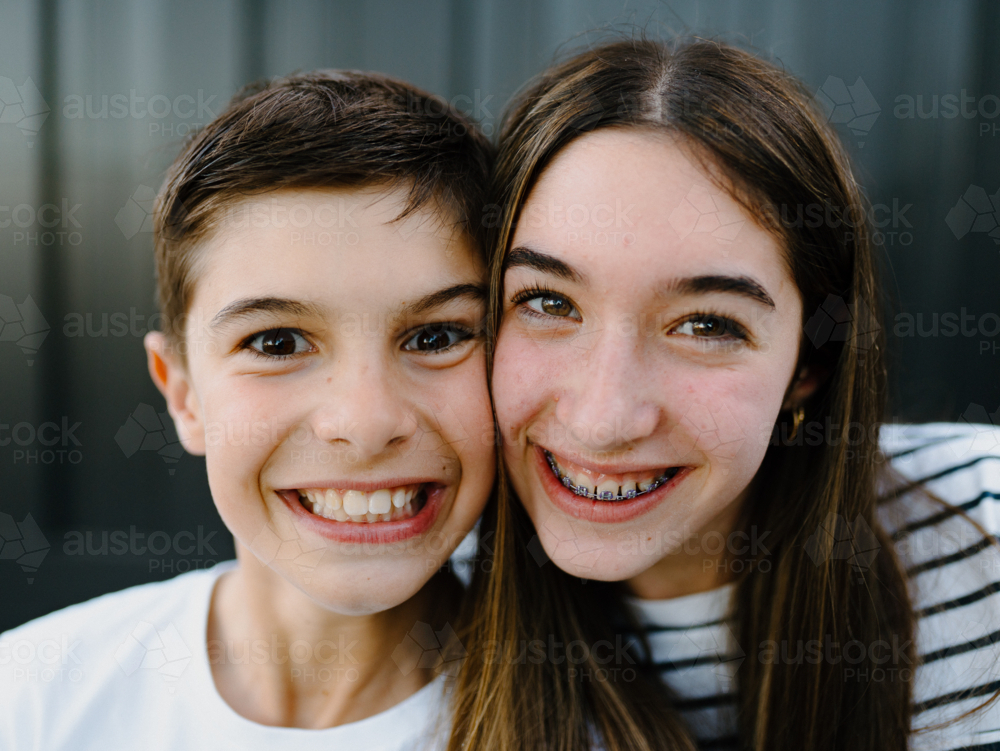 Closeup of brother and sister smiling at the camera. - Australian Stock Image