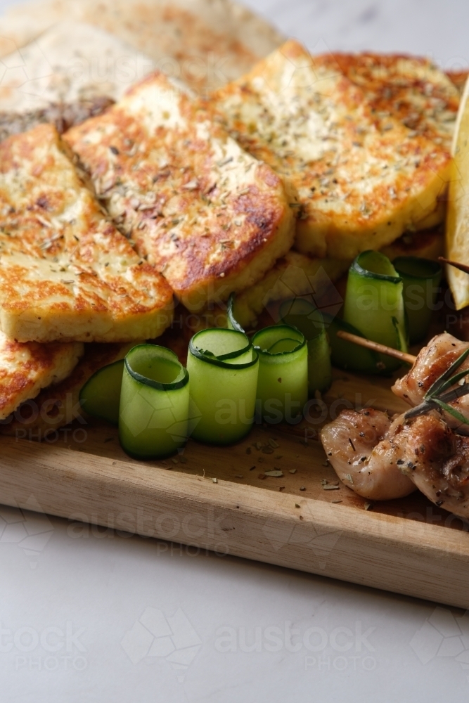 Closeup of seared halloumi cheese with thin slices of cucumber rolled up served on a wooden board - Australian Stock Image