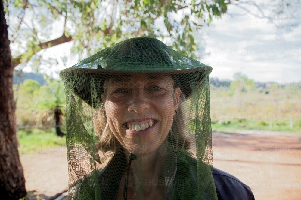 Closeup of woman smiling and wearing a fly net over her face in the outback - Australian Stock Image