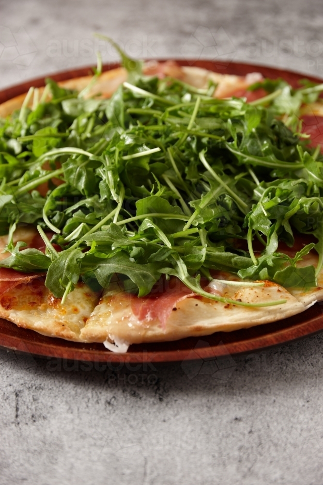Closeup of Prosciutto Arugula pizza on a wooden board - Australian Stock Image