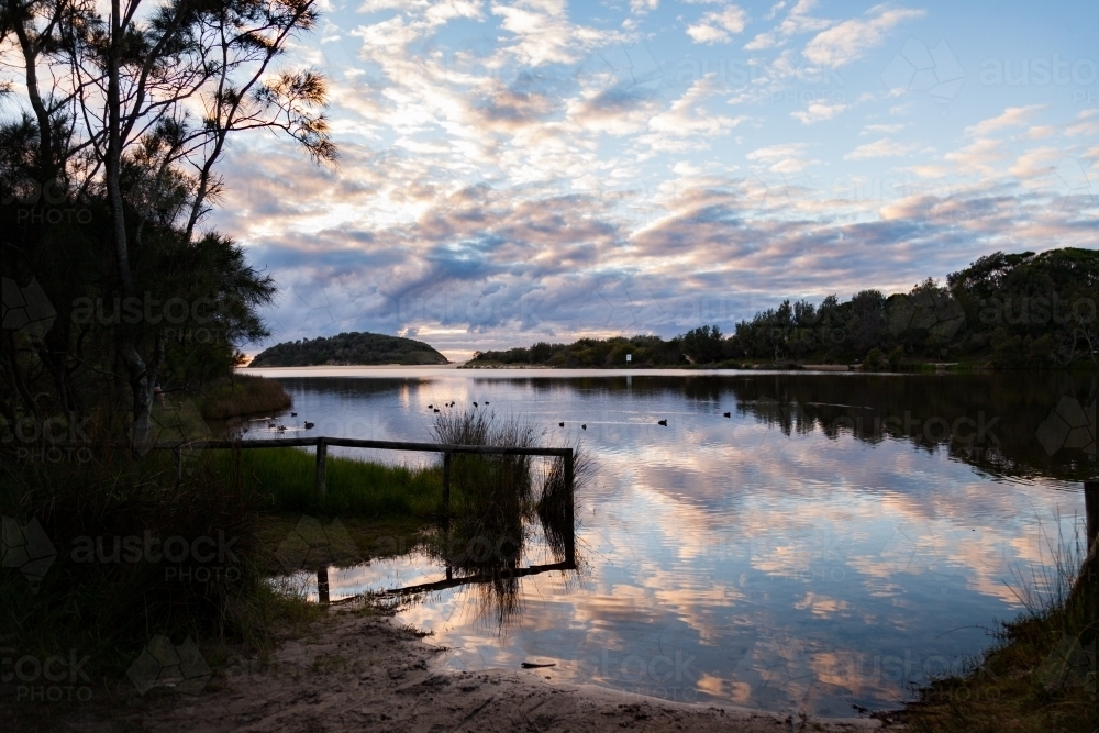Clouds reflected in lake beside ocean at dawn - Australian Stock Image