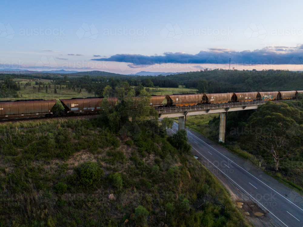 Coal train full of coal crossing over railway bridge over rural road at dusk - Australian Stock Image