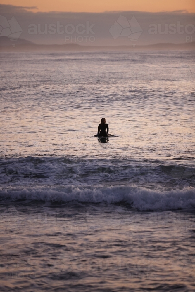Surfer waiting on ocean on sunrise - Australian Stock Image