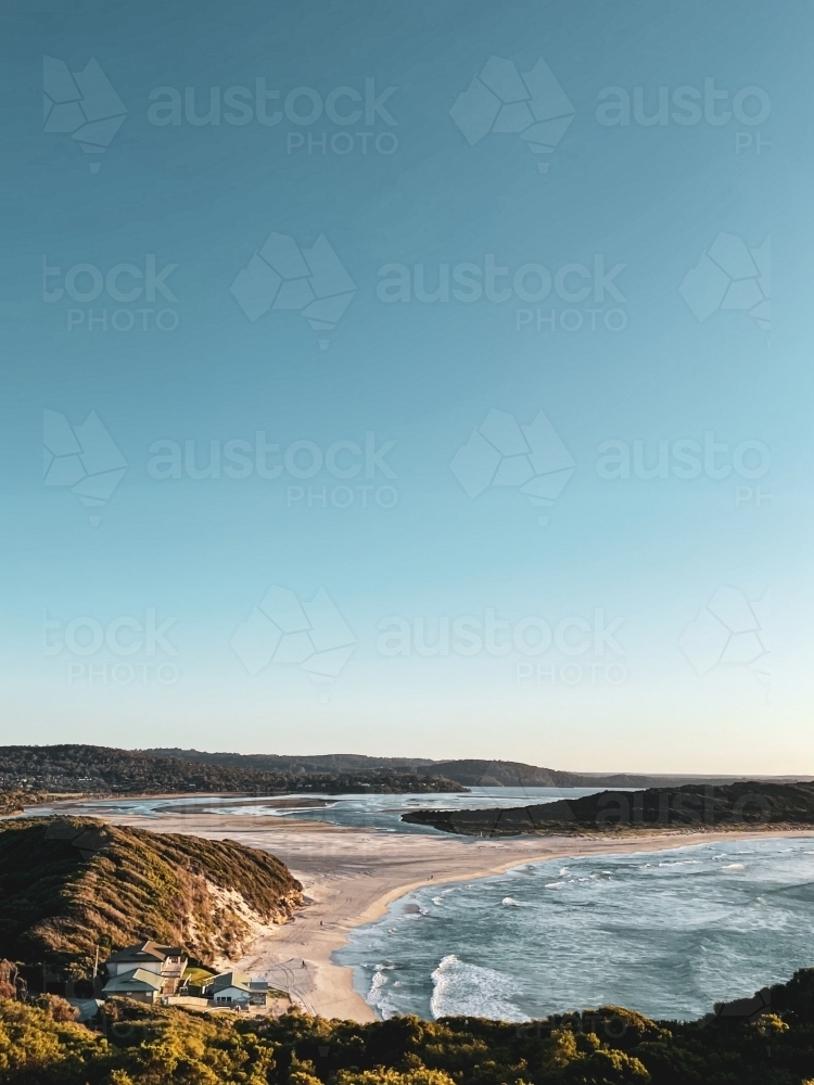 Coastal long shot of bay meeting river mouth with surf club buildings on beach - Australian Stock Image