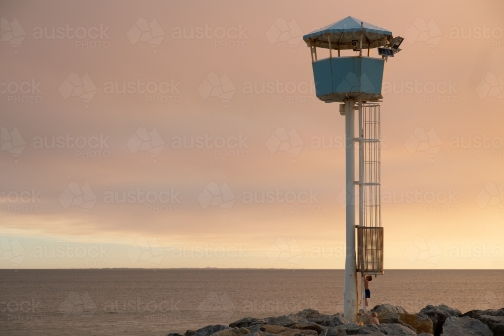 Coastal Lookout tower on groyne being climbed by young boy with dramatic sunset and ocean background - Australian Stock Image