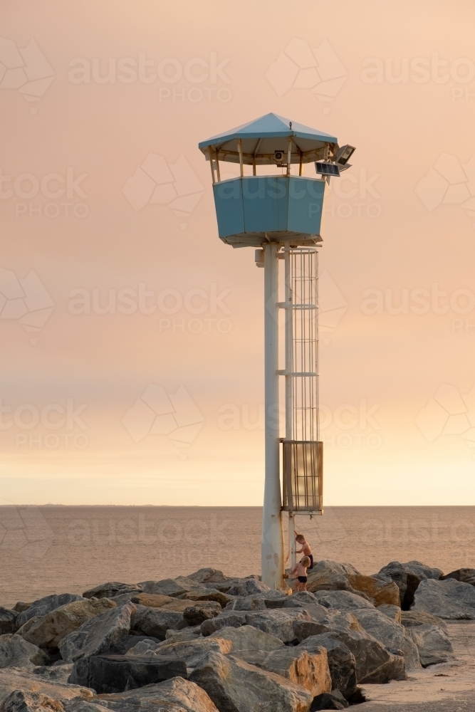 Coastal Lookout tower on groyne being climbed by young boy with dramatic sunset and ocean background - Australian Stock Image