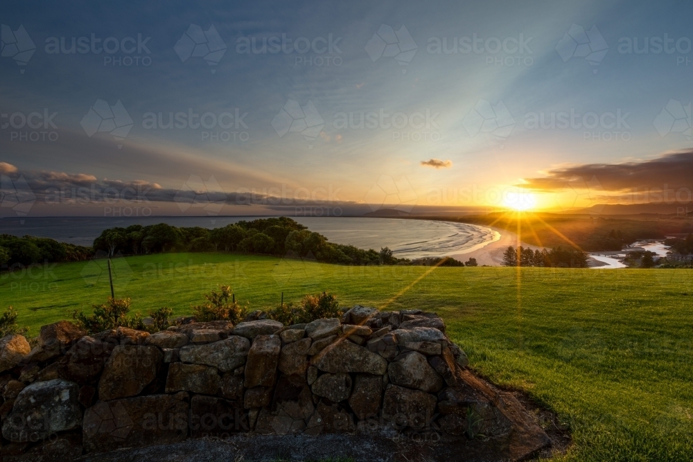 Coastal sunset landscape with rock wall, lush grass and beach - Australian Stock Image